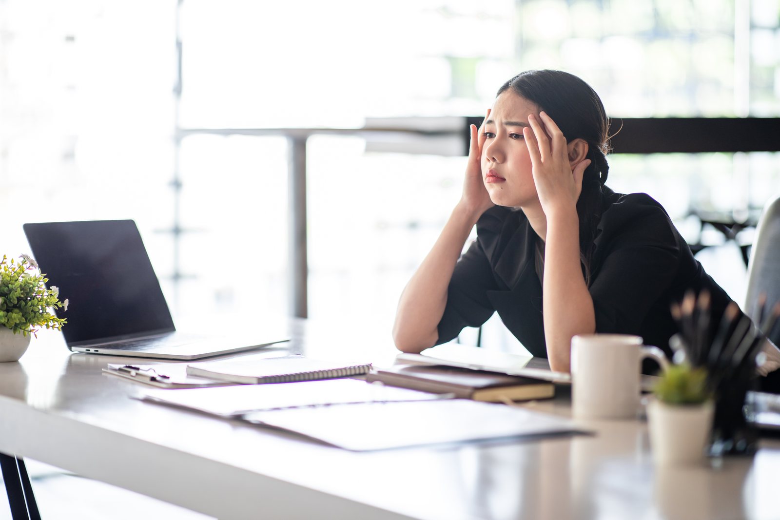 A woman at a desk with her head in her hands, exhausted