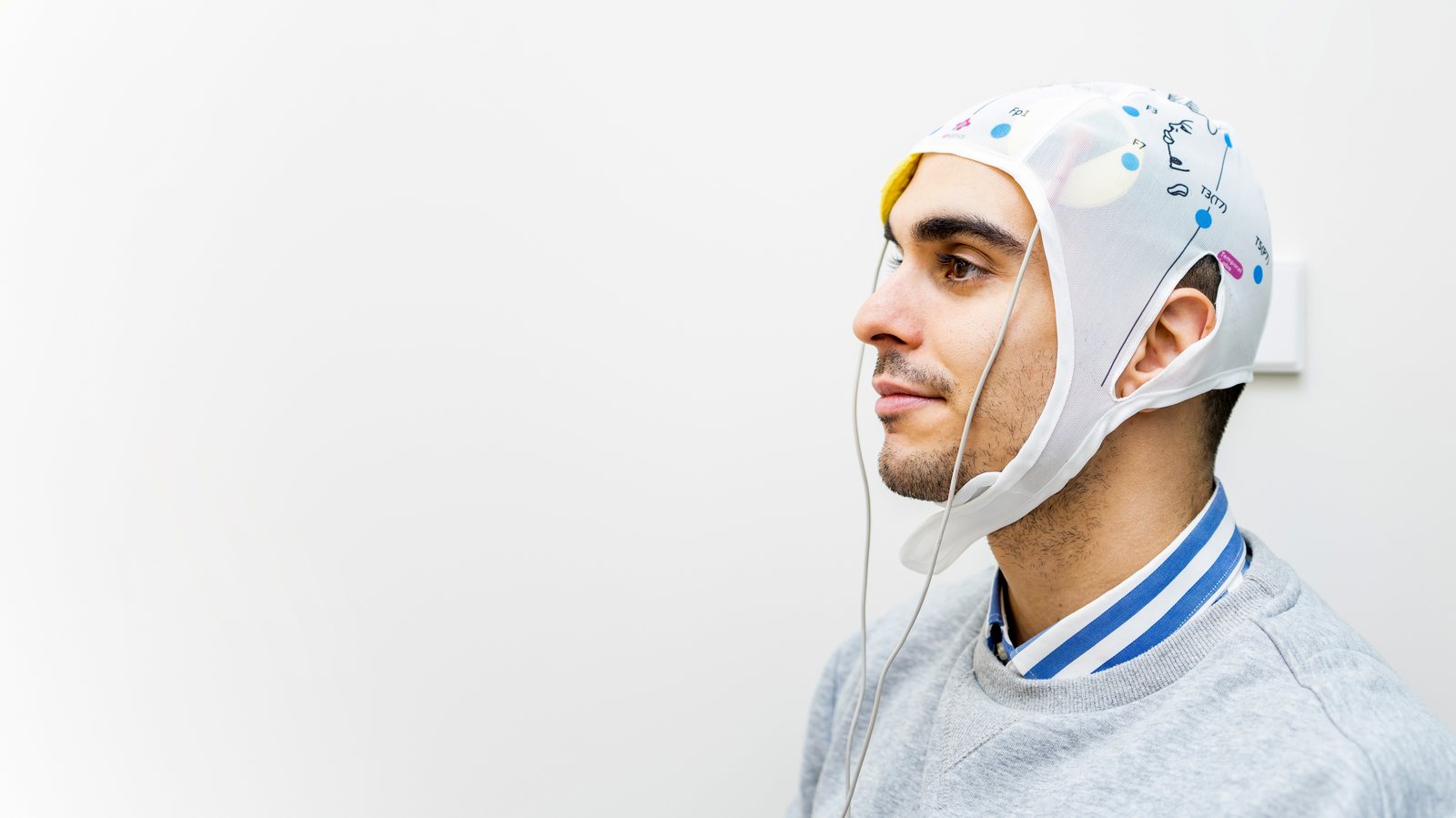 A man at home wearing a tDCS headband and holding the stimulator during a session